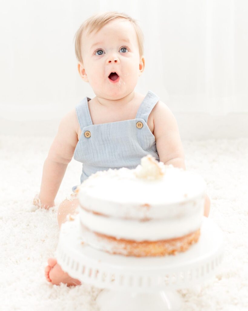 Baby boy shocked by his big cake at his birthday cake smash session taken by Brooke Leigh Photography , Plymouth Michigan Newborn Photographer at Studio Neue